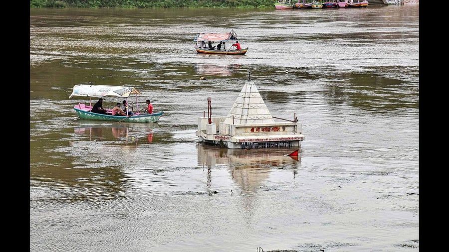 People ride boats on Narmada river near a submerged temple, following heavy rainfall. Credits: PTI Photo