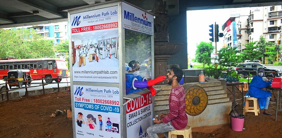 A medic collects a sample from a man for Covid-19 test from a swab collection booth under Kharghar flyover, in Navi Mumbai. Credits: PTI