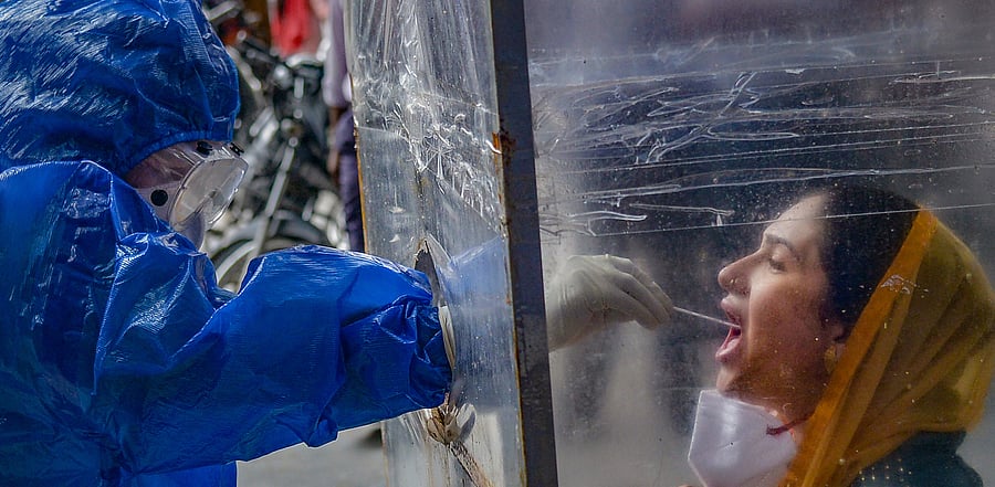 A medic collects samples from a woman for COVID-19 test, as coronavirus cases surge across the country, in Ajmer. Credit: PTI