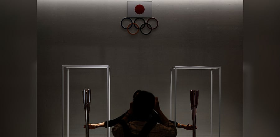 A visitor poses for pictures with the 2020 Tokyo Olympic relay torch (L) and Paralympic relay torch (R) at the Olympic Museum in Tokyo. Credit: AFP