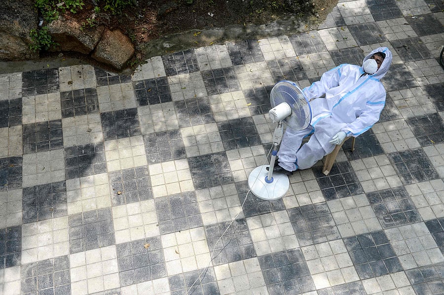 A health worker wearing a Personal Protective Equipment (PPE) suit takes a break sitting in front of a fan while waiting for to collect swab samples. Credits: AFP Photo