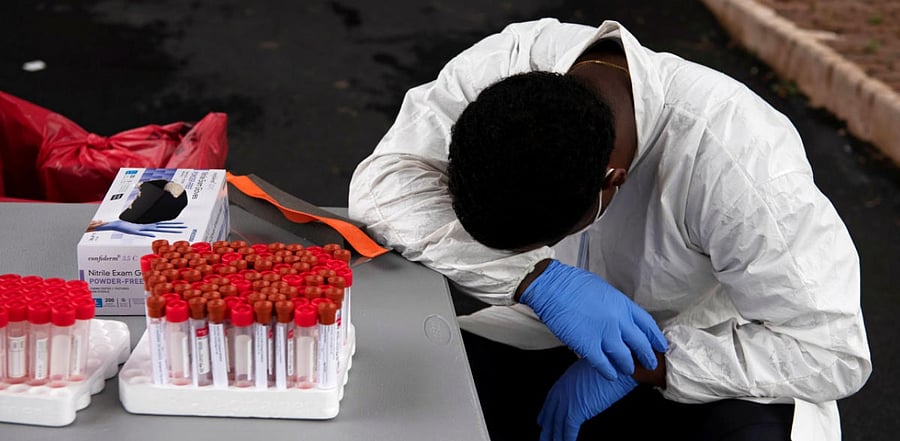 Overheated, a healthcare worker takes a break as people wait in their vehicles in long lines for the coronavirus disease testing. Credit: Reuters
