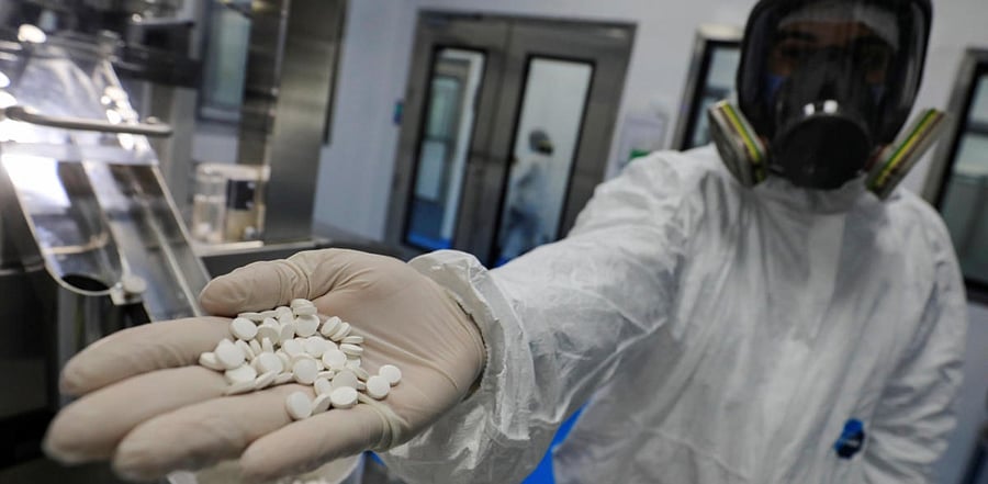 A lab technician wears a full-face mask and a protective suit holds tablets of investigational coronavirus disease treatment drug "Favipiravir". Credit: Reuters