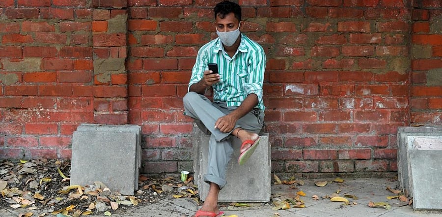 A man wearing a facemask as a preventive measure against the coronavirus, checks his mobile phone along the roadside. Credit: AFP