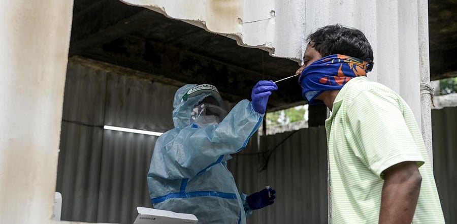 A health worker (L) wearing personal protective equipment (PPE) collects a swab sample from a resident for a coronavirus test at a temporarory collection centre. Credit: AFP