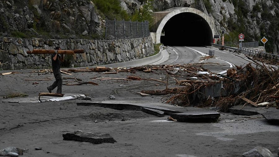 A man carries wood on October 6, 2020 on the damaged road leading to Breil-sur-Roya, a French village close to the Italian border, where houses were buried in mud and turned-over cars were stuck in the riverbed following heavy rains and floods. Credit: AFP.