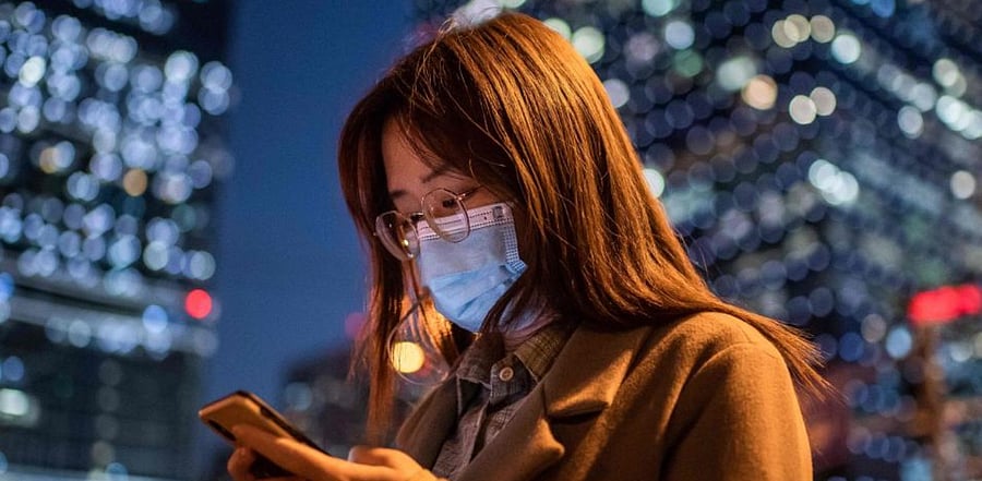 A woman wearing a face mask as a preventive measure against the Covid-19 coronavirus looks at her mobile phone. Credit: AFP