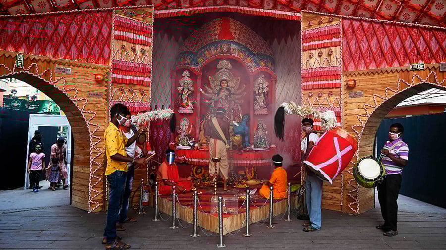 A Hindu priest (C) performs 'Arti' in front of a statue of the ten-handed Hindu Goddess Durga inside a makeshift worship place as traditional drummers perform during the Durga Puja festival in Kolkata. Credits: AFP Photo