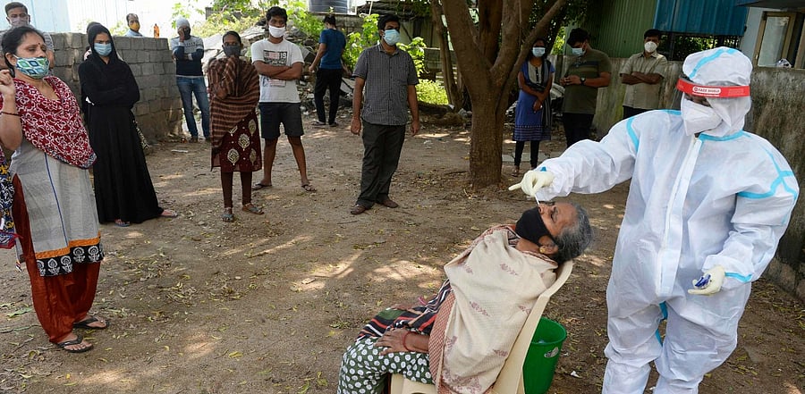 Residents watch as a health worker collects a swab sample from a woman to test for the Covid-19. Credit: AFP Photo