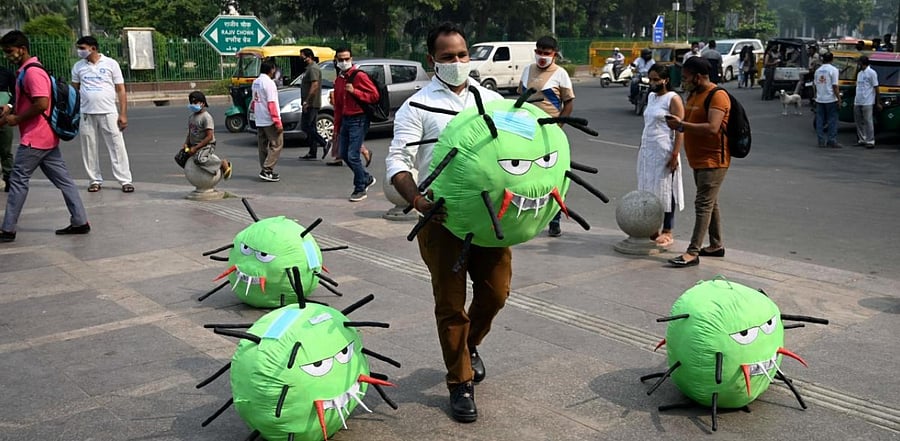 An officer from the district magistrate office holds a Covid-19 coronavirus-themed mascot in a market area during an awareness campaign against coronavirus and rising air pollution levels in New Delhi on October 26, 2020. Credit: AFP Photo