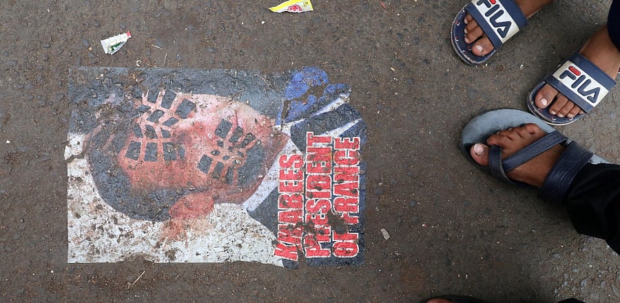 People stand next to a defaced poster of France's President Emmanuel Macron on a road as a mark of a protest against the publications of a cartoon of Prophet Mohammad in France and Macron's comments, in Mumbai. Credit: Reuters Photo