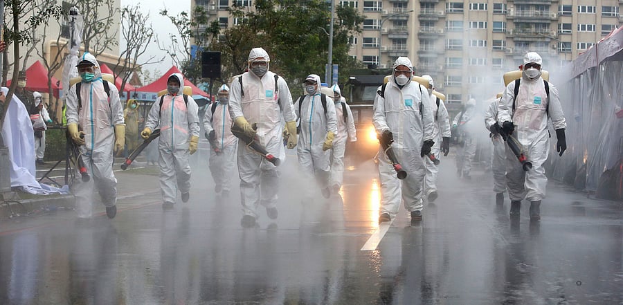 Taiwanese army soldiers wearing protective suits spray disinfectant over a road during a drill to prevent community cluster infection, in New Taipei City, Taiwan. Credit: AP