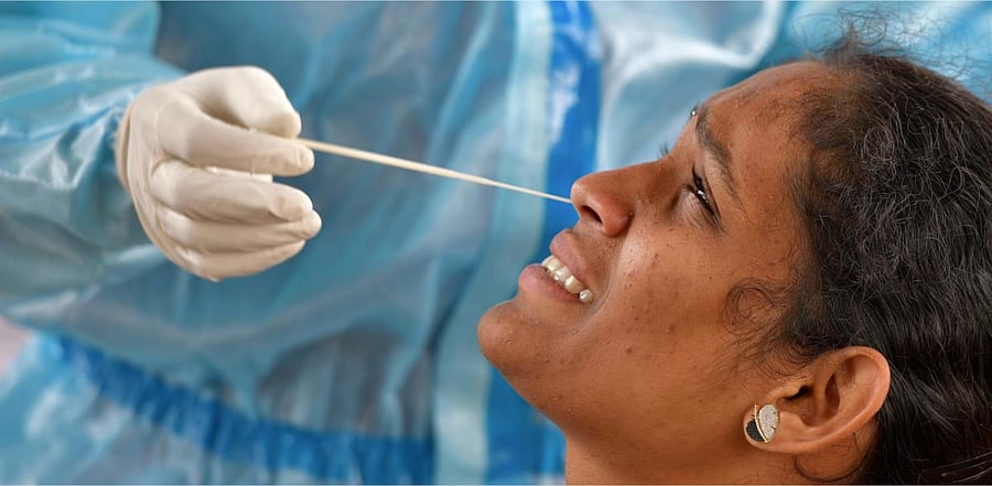 A health worker conducts swab test on a woman at a mobile Covid-19 coronavirus testing clinic at a bus stand in Bangalore. Credit: AFP