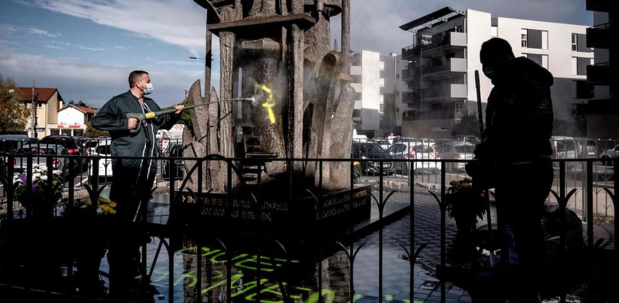 A man cleans the memorial for the Armenian genocide in Decines-Charpieu, near Lyon, on November 1, 2020 where pro-Turkish yellow letters graffiti tags have been painted overnight. Credit: AFP