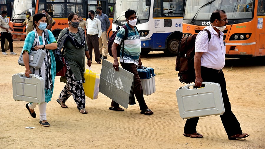 Polling officials carry EVMs and VVPATs as they leave for their respective booths ahead of Rajarajeshwari Nagar constituency by-polls. Credits: PTI Photo