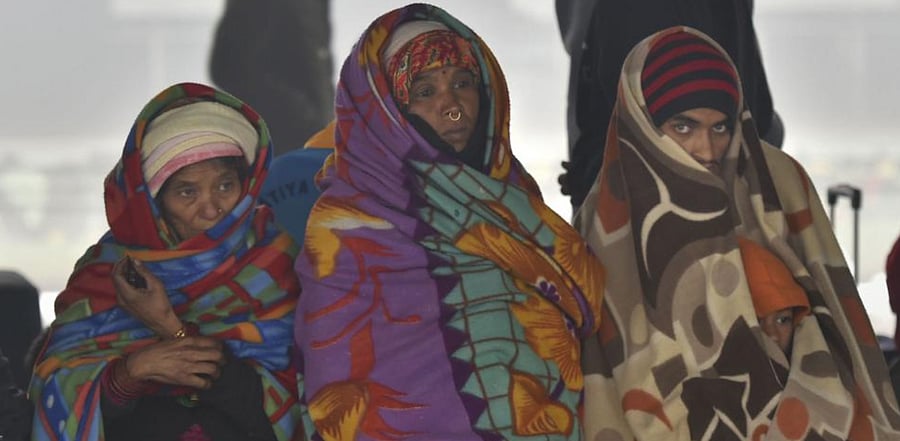 Passengers wrapped in blankets wait for their trains at a platform at the New Delhi railway station, during a cold and foggy morning in New Delhi. Credit: PTI File Photo