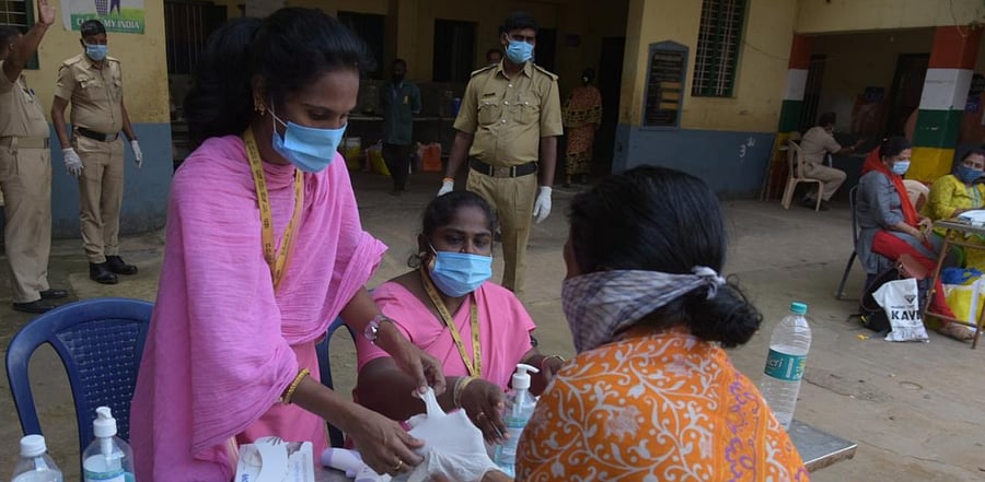 A pplling booth assistant helps an old woman wear gloves at a booth during the Rajarajeshwari Nagar bypolls. Credit: DH.