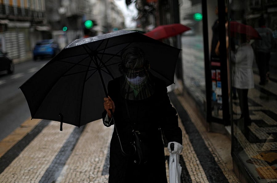 A woman wearing a face mask and a face shield protects herself from the rain with an umbrella during the coronavirus outbreak in Lisbon. Credit: Reuters
