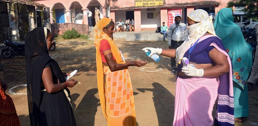 A woman sprays sanitizer on a voter's hand as she and others wait in a queue to cast their vote outside a polling booth during the state assembly election, at a village on the outskirts of Patna. (Reuters)