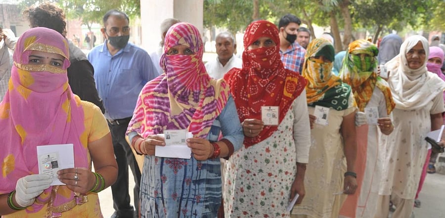Voters show their ID cards as they stand in a queue to cast their votes for the state by-polls, amid the coronavirus pandemic, at Baroda. Credit: PTI