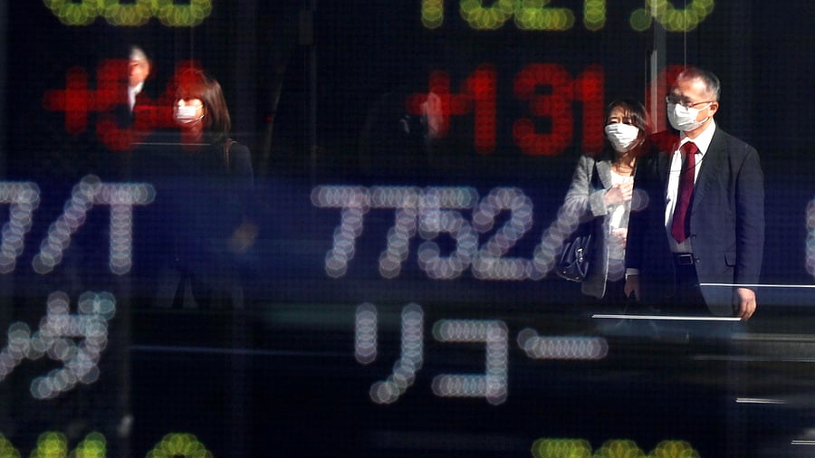 Passersby wearing protective face masks are reflected on a stock quotation board outside a brokerage, amid the coronavirus disease (Covid-19) outbreak. Credits: Reuters Photo