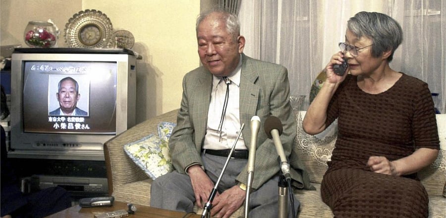 Japanese physicist Masatoshi Koshiba sits with his wife Keiko Koshiba answering a congratulatory phone call as TV news reports his winning of the 2002 Nobel Prize in Physics at his home in Tokyo. Credit: File AP Photo