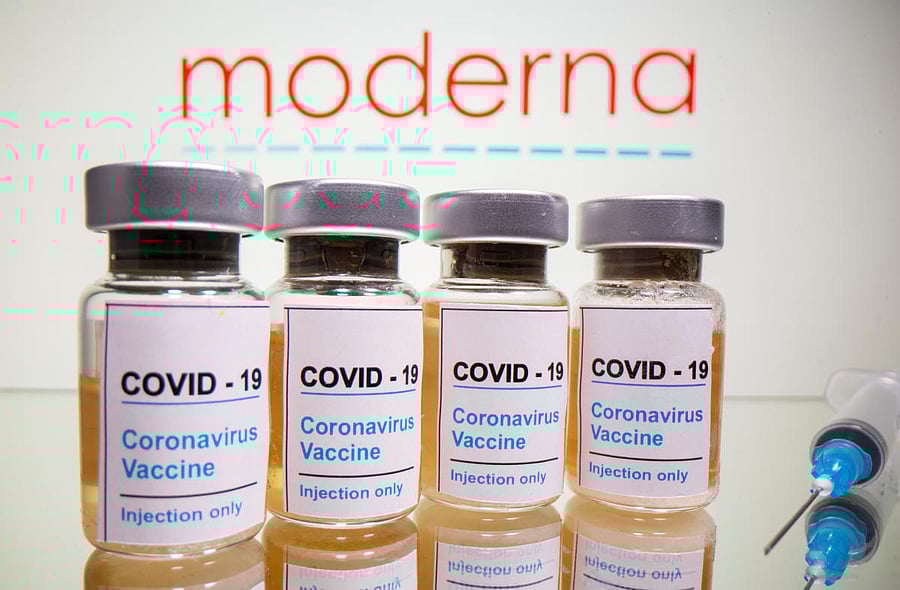 Vials with a sticker reading, "Covid-19 / Coronavirus vaccine / Injection only" and a medical syringe are seen in front of a displayed Moderna logo. Credit: Reuters