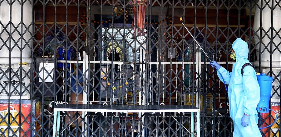 An employee, wearing a PPE kit, sanitizes the premises of a Hindu temple in Mumbai. Credit: PTI Photo
