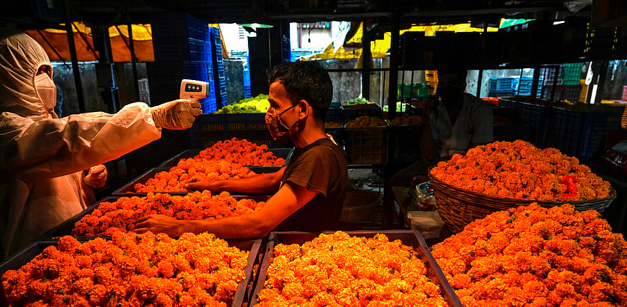 A health worker (L) checks the body temperature from a shopkeeper during a Covid-19 coronavirus RT PCR and Rapid Antigen test at a flower market in Mumbai. Credit: AFP