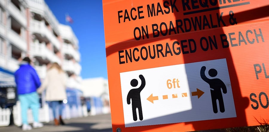 A couple holding hands walks past a directive stating 6 feet of physical distancing while on the boardwalk. Credit: AFP Photo