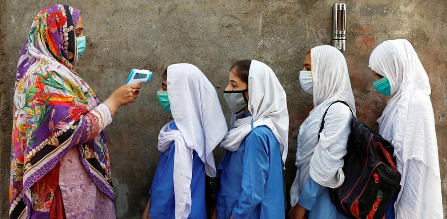 Students wear protective face masks as they have their temperature checked before entering a class, after the government allowed the reopening of schools from grade six to eight amid coronavirus, in Peshawar. Credit: Reuters Photo