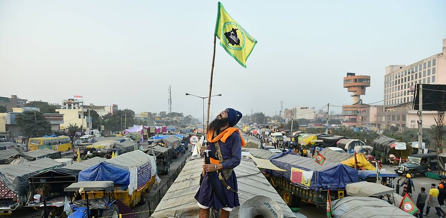 A farmer holding a flag stands on top of a truck during the ongoing protest against the Center's new farm laws, at Singhu border in New Delhi. Credit: PTI Photo