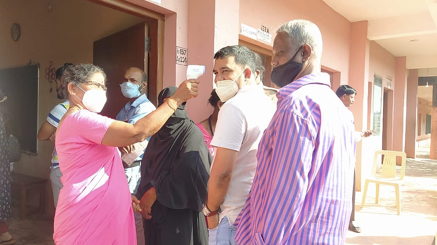 Asha worker checks the body temperature of voters at Talapady Gram Panchayat in Mangaluru taluk. Credit: DH Photo