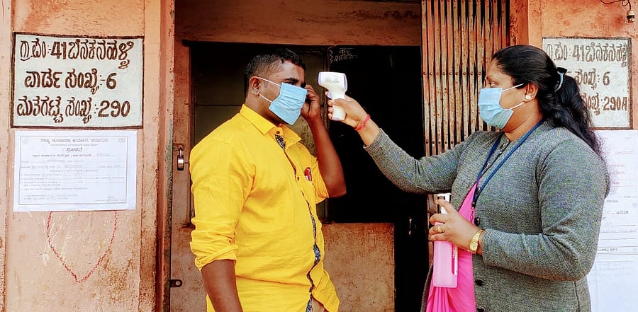 Election personnel checking body temperature of a voter during the first phase of Gram Panchayat elections at polling station at Jyoti Nagar in Belagavi coming under Benkanhalli Gram Panchayat on Tuesday. Credit: Special arrangement