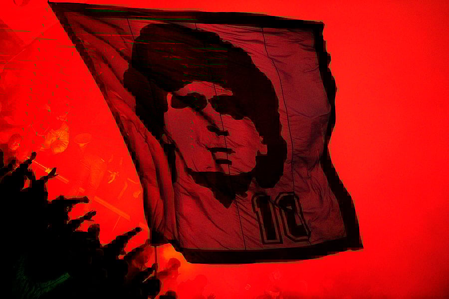 SSC Napoli's supporters wave a flag bearing a portrait of football legend Argentinian Diego Maradona during the Serie A football match SSC Napoli vs Inter Milan at San Paolo Stadium in Naples. - Diego Maradona's death on November 25, 2020 shook the world of sport. The surprise and pain over the death of the football troubled genius at the age of 60 reinforced his myth and multiplied the tributes that seek to immortalize him. Credit: AFP Photo