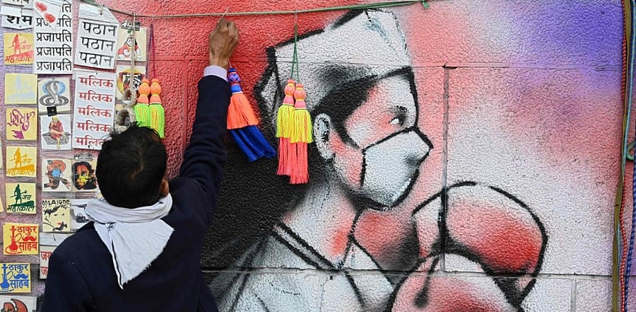 A vendor prepares to set up his roadside stall in front of a mural representing a frontline warrior of the Covid-19 coronavirus, painted on a wall in New Delhi. Credit: AFP.