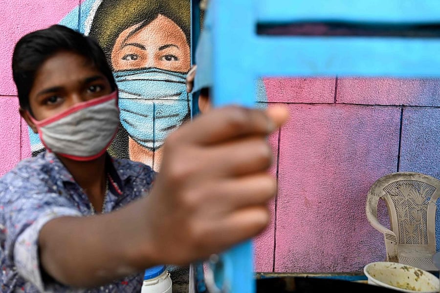 A vendor watches as he waits for customers at his roadside eatery stall in front of a mural representing a frontline warrior of the Covid-19 painted on a wall in New Delhi. Credit: AFP. 