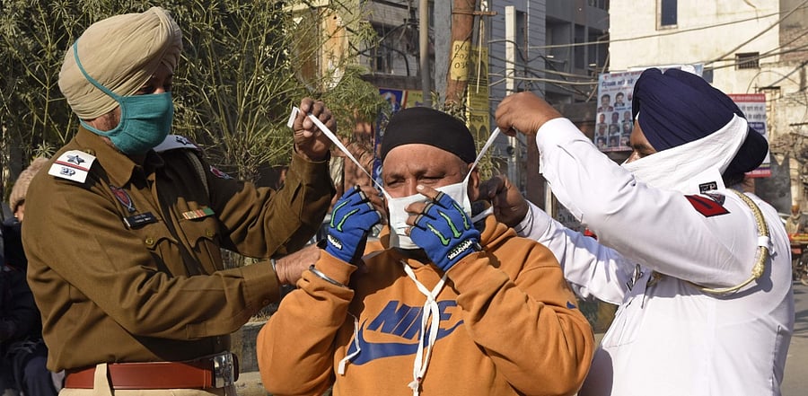 INDIA-HEALTH-VIRUS Policemen prepare to tie a mask on the face of a motorbike rider as they distribute facemasks to commuters during an awareness campaign for Covid-19. Credit: AFP Photo