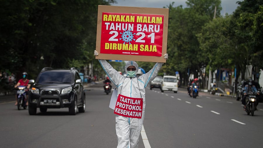 A man wearing protective gear holds a sign reading “Celebrate New Year's Eve 2021 at home” and “adhere to health protocols” at the Solo, Central Java Province. Credit: Reuters Photo