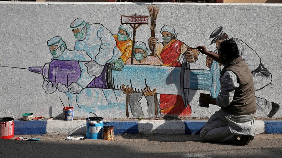 A man applies finishing touches to graffiti representing a vaccine, amidst the spread of coronavirus disease in Kolkata. Credit: Reuters Photo