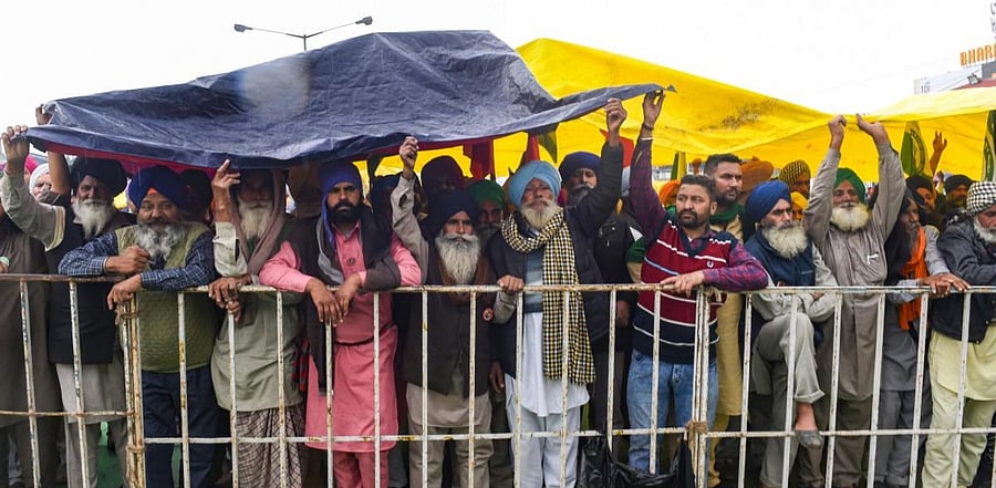 Farmers take cover from the rain during their ongoing protest against new farm laws, at Singhu border, in New Delhi, Monday, Jan. 4, 2021. Credit: PTI Photo