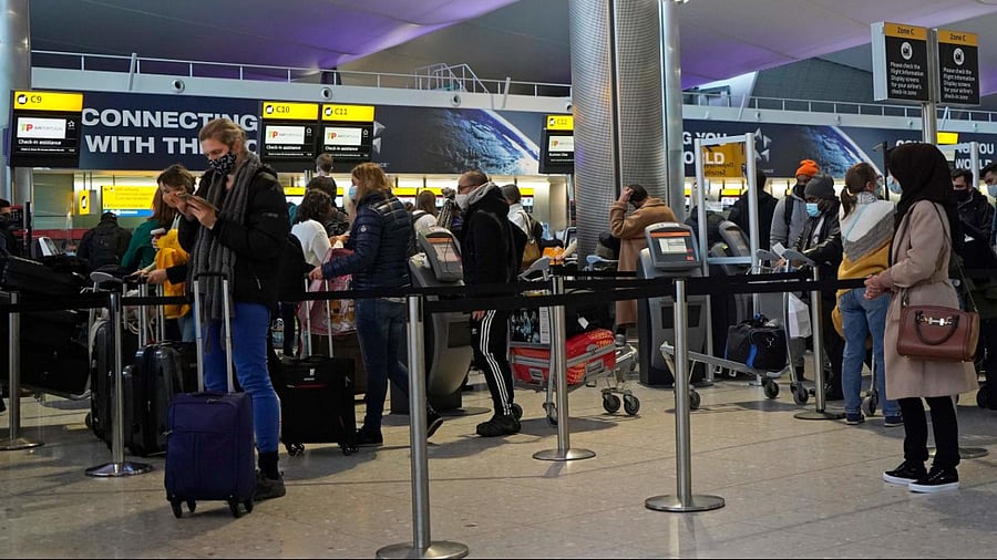 Customers wearing face covers queue at a TAP Air Portugal check-in desk in the departures hall at Terminal 2 of Heathrow Airport in west London. Credit: AFP File Photo