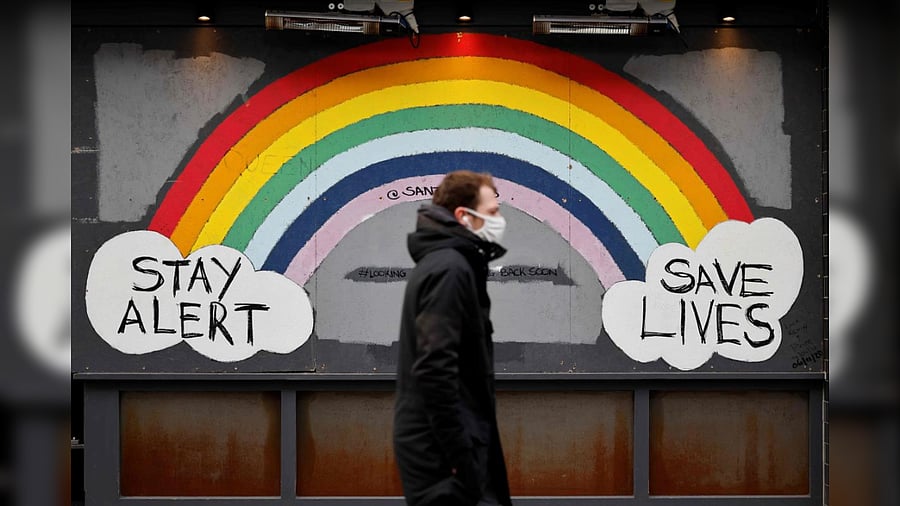 A man wearing a face mask as a precautionary measure against COVID-19, walks past graffiti in the window of a closed restaurant on Old Compton Street in Soho, central London on January 15, 2021, during the third nationwide coronavirus lockdown. Credit: AFP Photo
