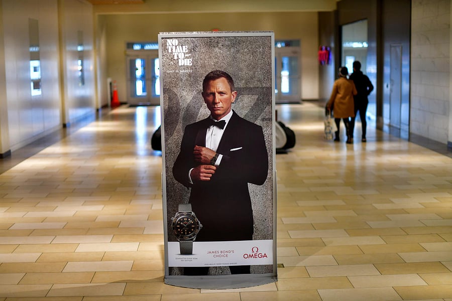 Shoppers walk past an advertisement for the upcoming James Bond film "NO TIME TO DIE" whose release has been delayed to October. Credit: Reuters. 