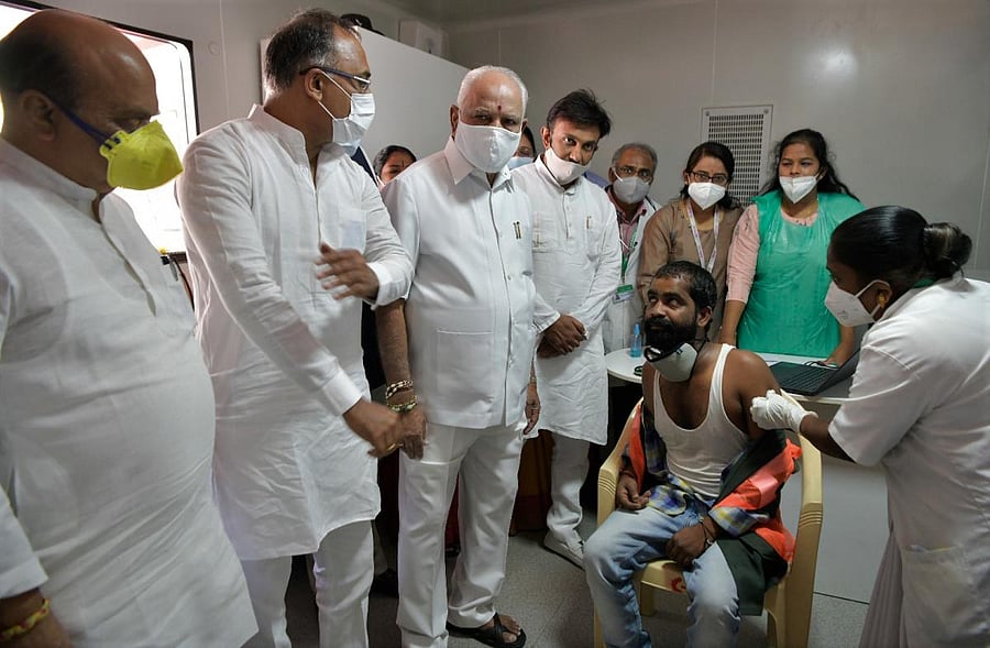 Pourakarmika Ramesh gets the Covid-19 jab at KC General Hospital, Malleswaram, in the presence of Chief Minister B S Yediyurappa, Health Minister Dr K Sudhakar, Home Minister Basavaraj Bommai and MLA Dinesh Gundu Rao on Monday. Credit: DH special arrangement
