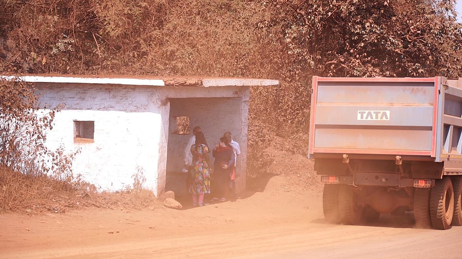 Passengers wait at a bus stop amid dust in Sandur. Credit: DH Photo