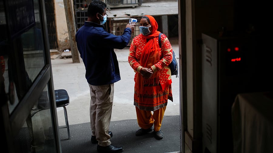 A man checks the temperature of a woman, outside a vaccination centre, in New Delhi, India. Credit: Reuters Photo