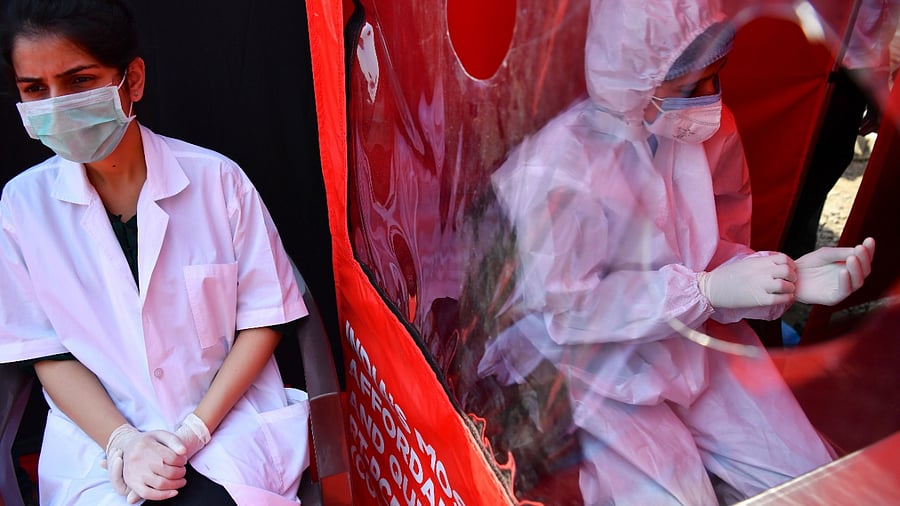 Health workers wait to take swab samples at a portable cabin of a mobile laboratory for conducting RT-PCR Covid-19 coronavirus tests in Mumbai on February 11, 2021. Credit: AFP Photo