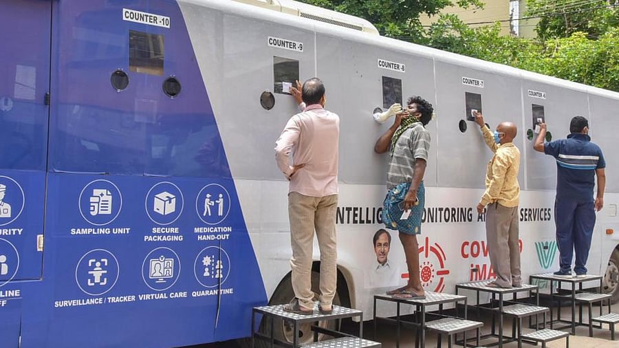 People stand near a Covid-19 mobile testing facility, at Jafarguda near Karwan in the old city of Hyderabad, Friday, July 31, 2020. Intelligent Monitoring Analysis Services Quarantine’ (iMASQ), the testing facilities are housed in specially designed buses, developed by Hyderabad-based Vera Smart Healthcare. Credit: PTI Photo