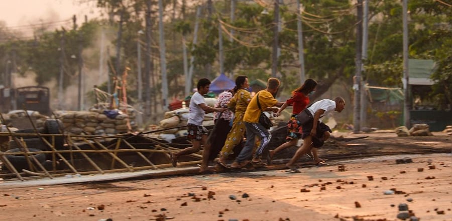 People run past makeshift barricades set up by protesters, during a crackdown by security forces on demonstrations against the military coup, in Hlaing Tharyar township in Yangon on March 14, 2021. Credit: AFP Photo